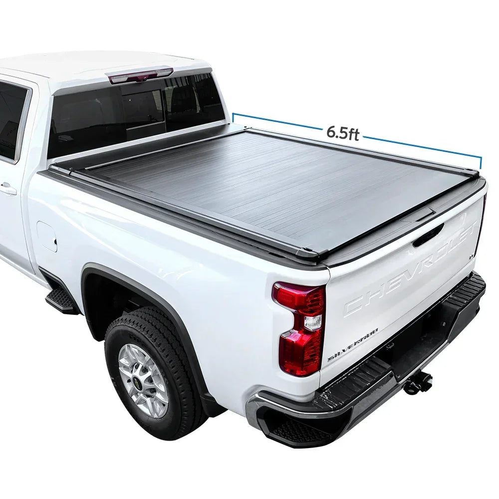 A retractable tonneau cover made of aluminum and plastic, installed on the bed of a white pickup truck.