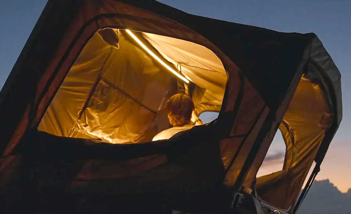 Two people inside a tent with a scenic view outside during sunset.