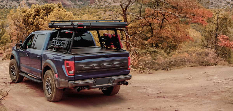 Blue pickup truck with roof rack on a dirt road in a forested area