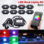 An 8-piece LED rock light kit shown on a white background, including eight black LED units, a black controller box with wiring, a smartphone displaying a color wheel app, and four inset images showing the lights glowing in red, blue, purple, and green. Text at the top reads 'LED Rock Lights Kit 8pcs'.