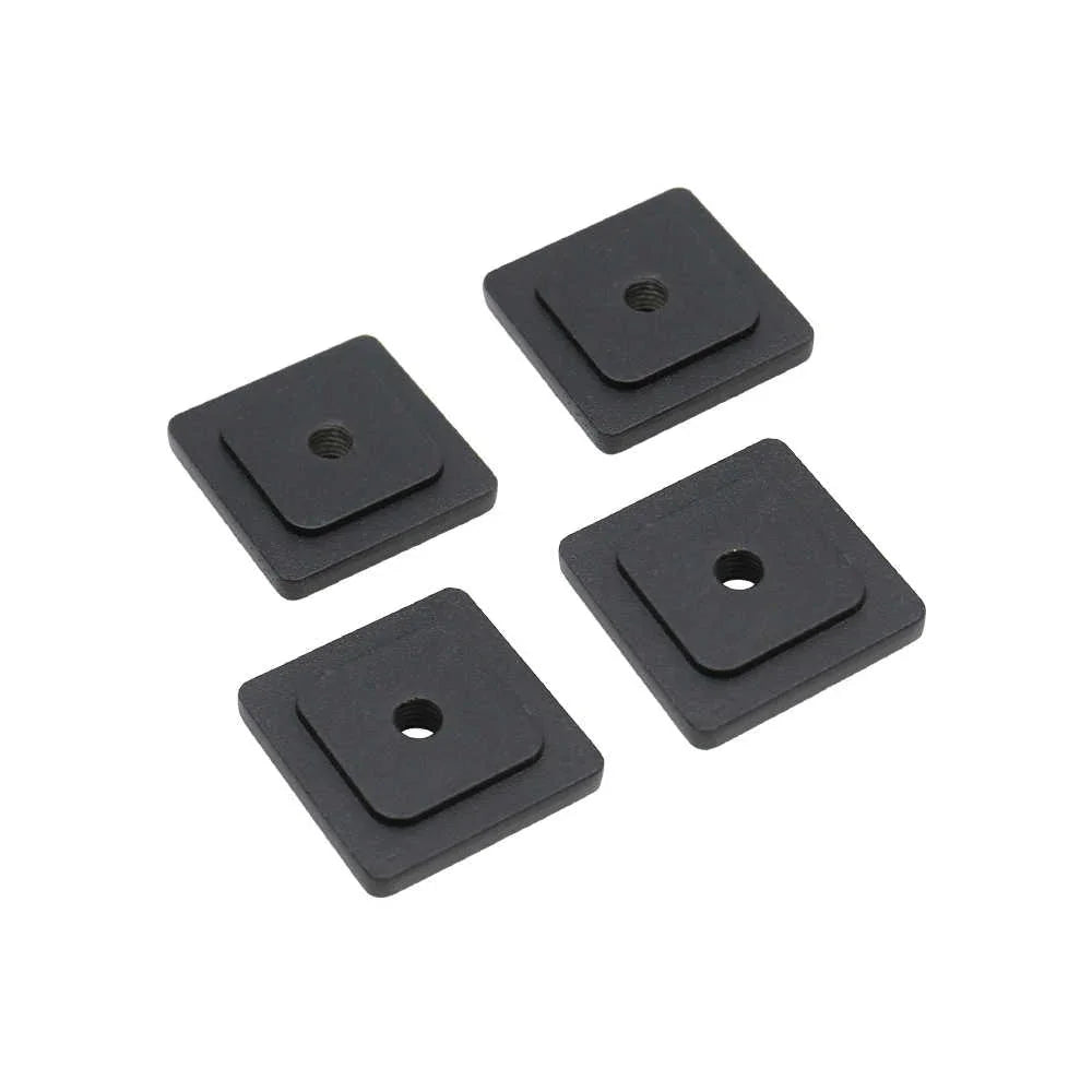 Four black square rubber washers with central holes on a white background