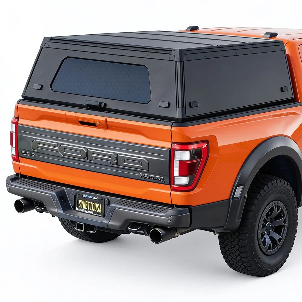 Black hardtop truck canopy installed on the bed of an orange Ford Raptor pickup truck, shown from a rear three-quarter angle against a white studio background.