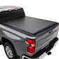 SYNETICUSA soft roll-up tonneau cover installed on the bed of a gray Chevrolet Silverado pickup truck, shown from a rear three-quarter angle against a white background.