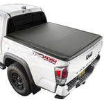White Tacoma truck with a black soft roll up tonneau cover on a white background