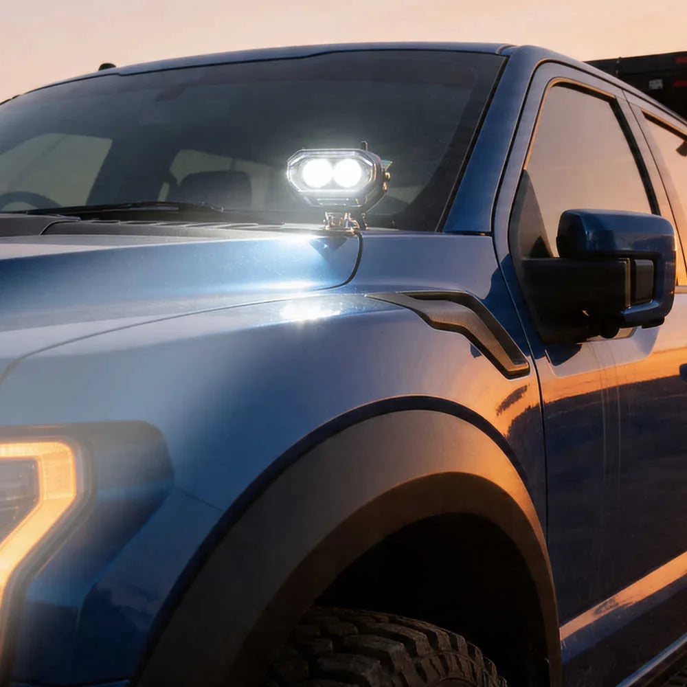 Close-up of a blue truck with a spot light on the hood during sunset.