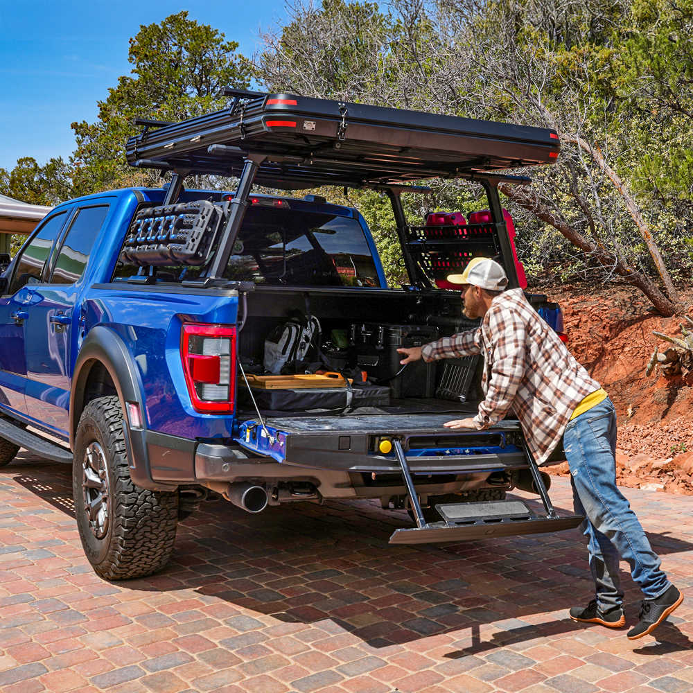 Blue Raptor installed syneticusa PRO quad pack with open cargo area and person loading items, surrounded by trees and natural landscape.
