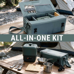 An outdoor camping cookware set displayed on a wooden table with a tent in the background. The set includes a large sage green carrying case, a matching multi-level pot, metal utensils, a cutting board, and cookware.