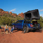 Blue Raptor with a dessert cruiser rooftop tent in a desert setting with two people sitting nearby.
