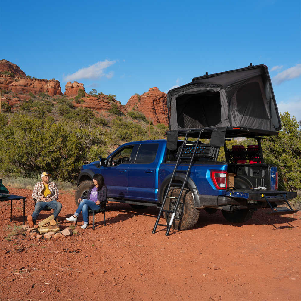 Blue Raptor with a dessert cruiser rooftop tent in a desert setting with two people sitting nearby.