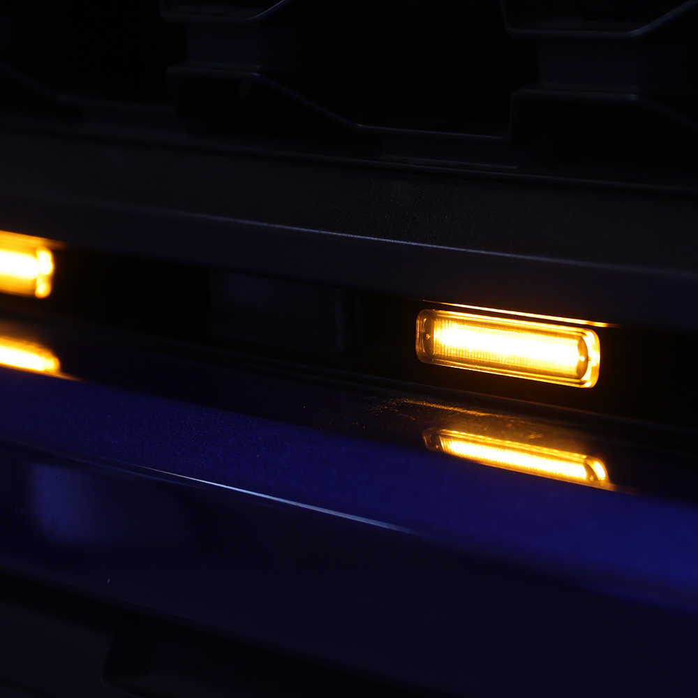 Close-up of a car's front bumper with illuminated amber grill lights in the dark.