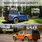 Promotional graphic for a truck canopy load capacity feature, showing two vehicles: a blue pickup truck with a black canopy in a forest with '1200lbs STATIC' text, and an orange pickup truck on a highway with a black canopy and '550lbs DYNAMIC' text.