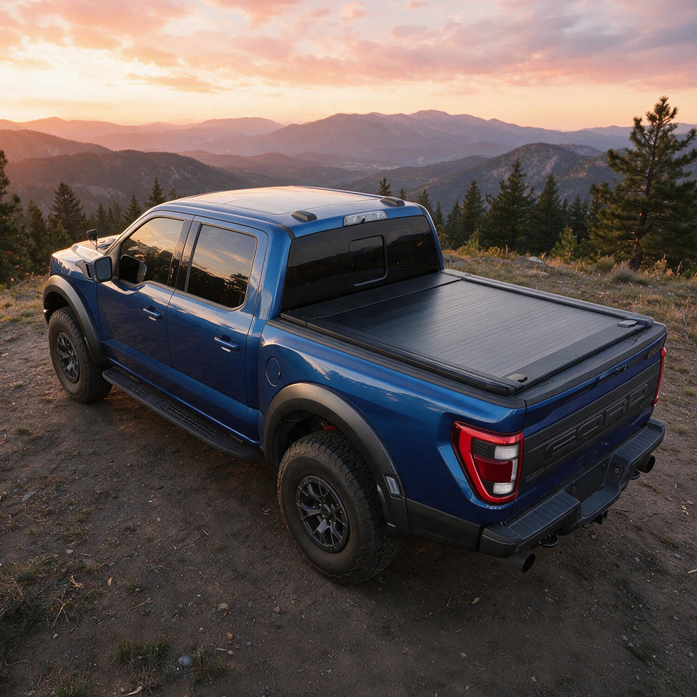A blue Ford pickup truck parked outdoors on a dirt trail with mountains and trees in the background at sunset. The truck bed is covered by a black tonneau-style cover.