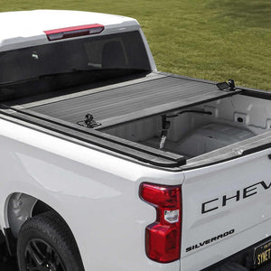 White Chevrolet Silverado truck with syneticusa tonneau cover on a grassy field