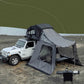 White Jeep with a rooftop tent and attached ground tent near a body of water.