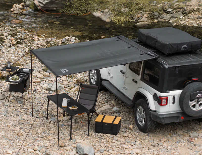 White SUV with a rooftop tent and outdoor furniture near a rocky stream.