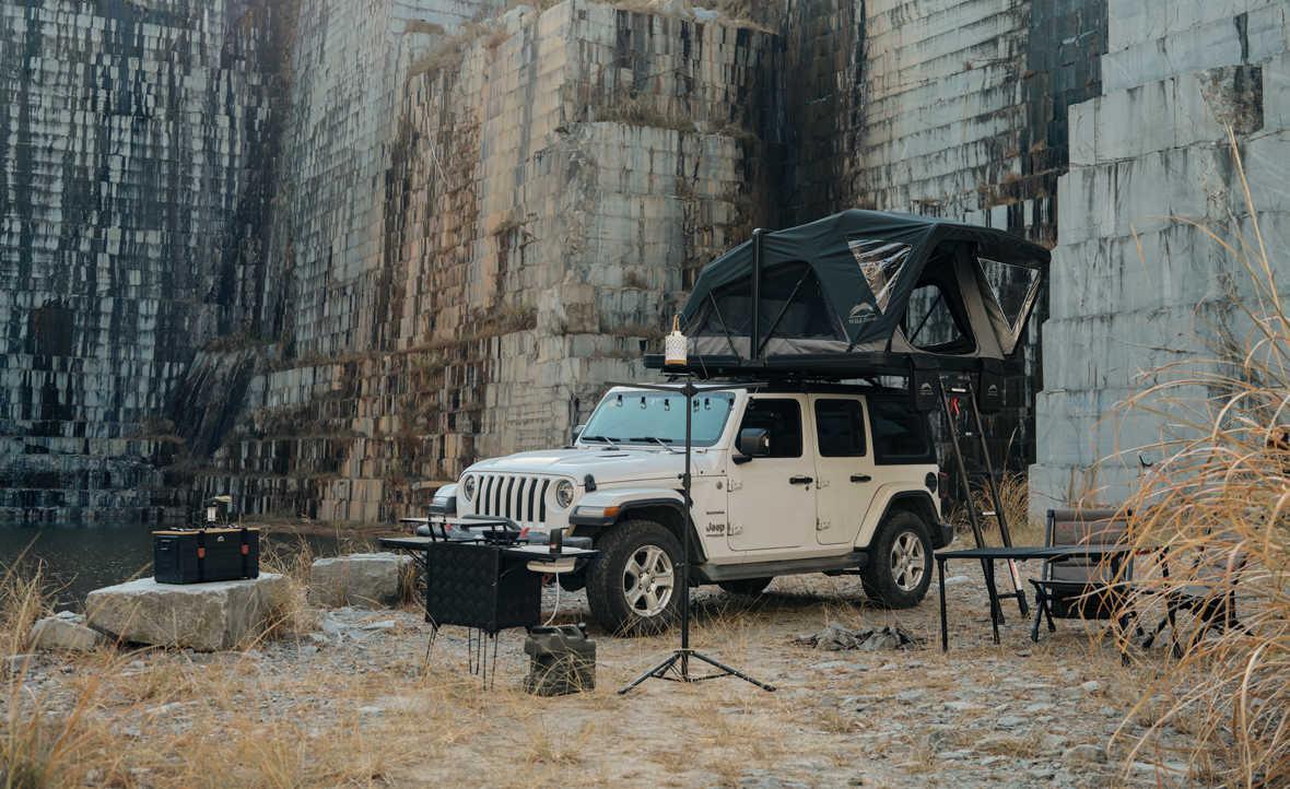 Jeep with a rooftop tent parked in front of a rocky wall