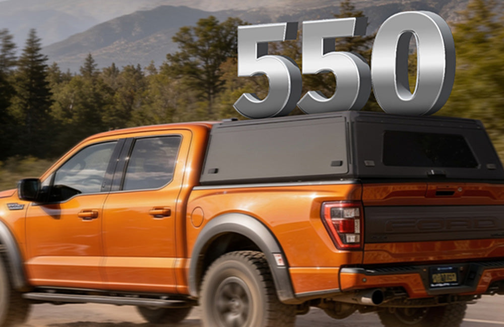 An orange Ford F-150 pickup truck is shown from the rear three-quarter angle in a real outdoor setting with trees and mountains in the background. Large metallic '550' text is overlaid above the truck bed canopy.