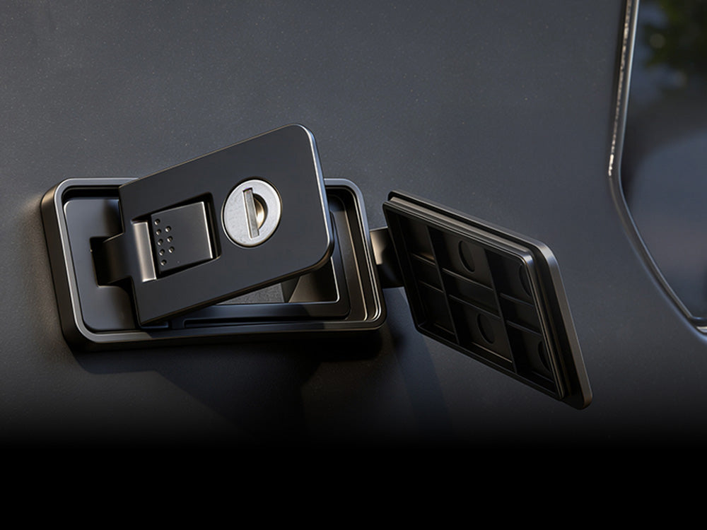 A close-up of a black fuel door latch and latch cover attached to a dark vehicle panel.