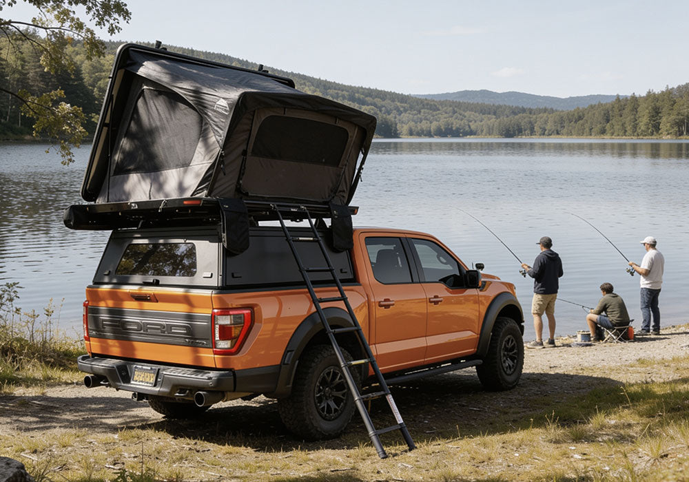 An orange Ford pickup truck parked by a lake with a rooftop tent open and a ladder extending from the back. Three people are standing and sitting on the shore nearby, fishing.