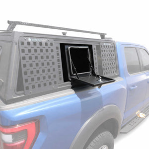 A blue pickup truck with a gray SyneticUSA branded hardtop canopy on the bed, shown from the rear three-quarter angle with the center hatch of the canopy open.
