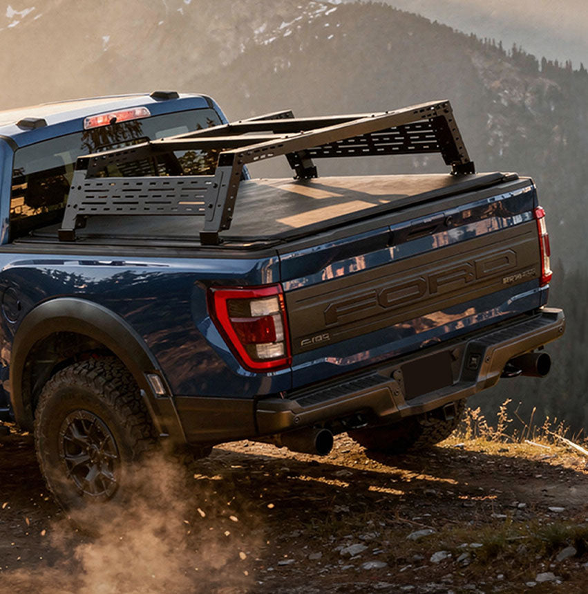 Blue Ford truck with a bed cover on a dirt road with mountains in the background