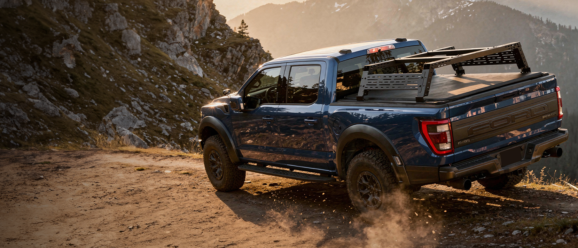 Blue pickup truck on a dirt road with mountains in the background