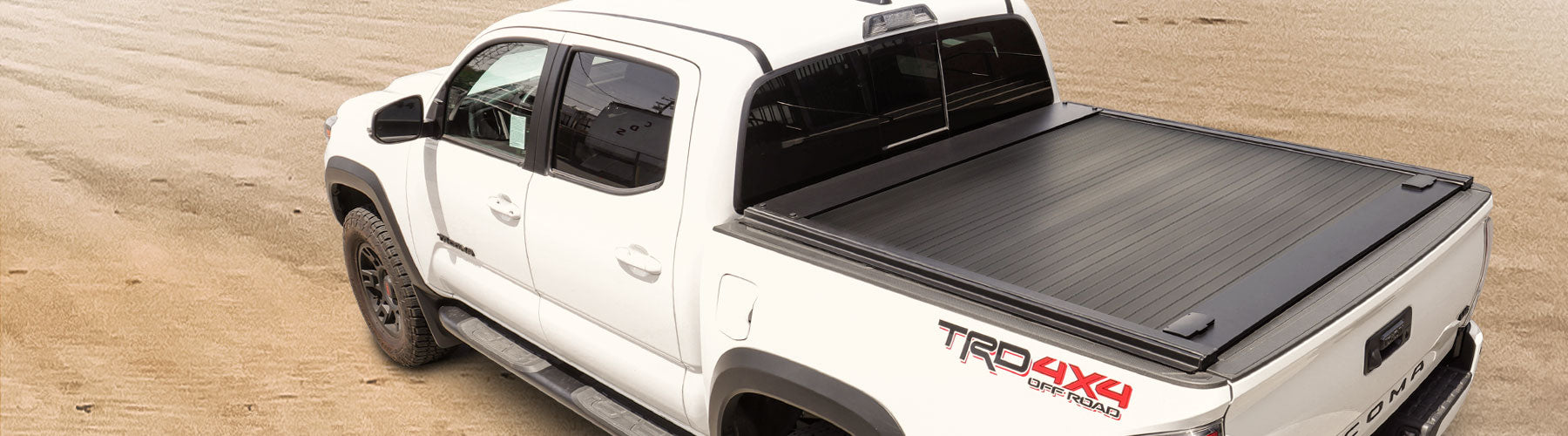 White Tacoma with a SYNETICUSA MB tonneau cover on a sandy background