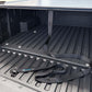 Black truck bed liner strap with a blue and white SYNTHETIC USA logo, laid out on the textured black bed liner of a pickup truck.
