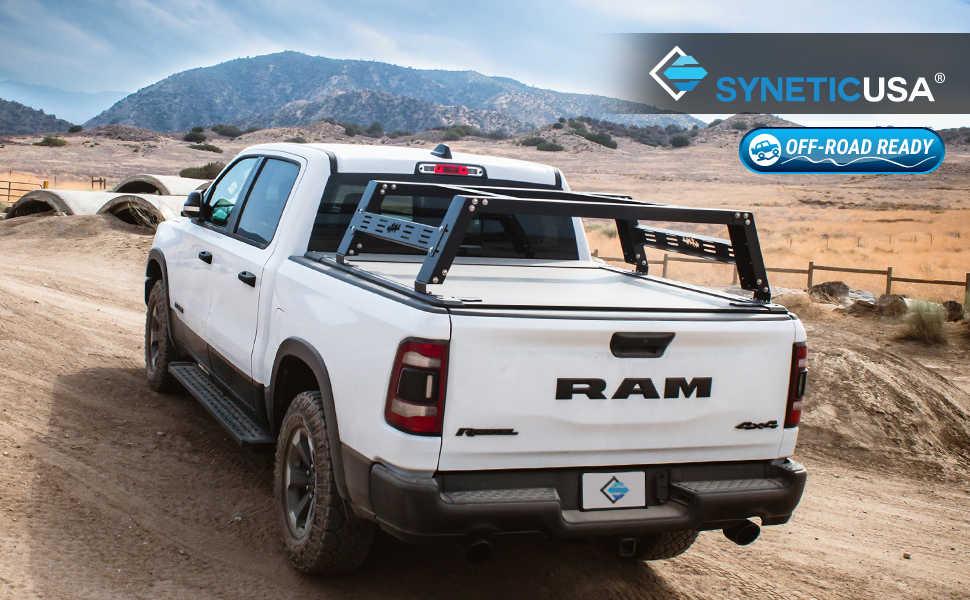 White RAM truck with a bed rack on a dirt road, featuring syneticusa branding.