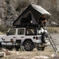 Person sitting on a ladder accessing a rooftop tent on a Jeep in a natural setting.
