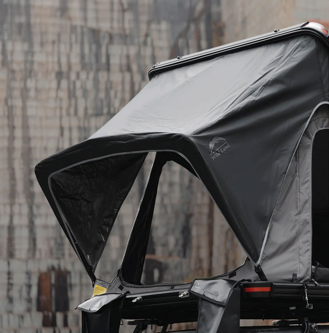 Black and gray awning attached to a vehicle with a blurred cityscape background