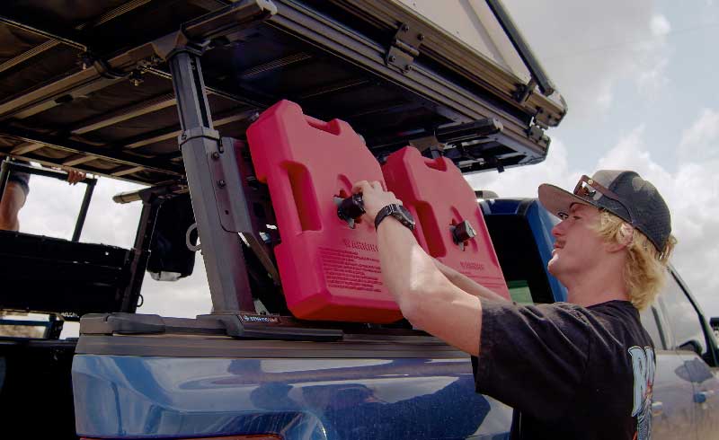 Person securing red gas cans on a vehicle's bed rack