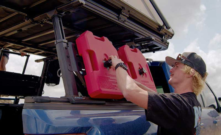 Person securing red gas cans on a vehicle's bed rack