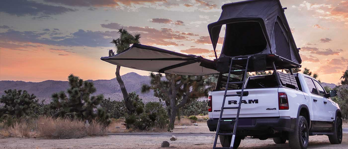 White RAM truck with a rooftop tent and extended awning in a desert landscape at sunset. wide angle