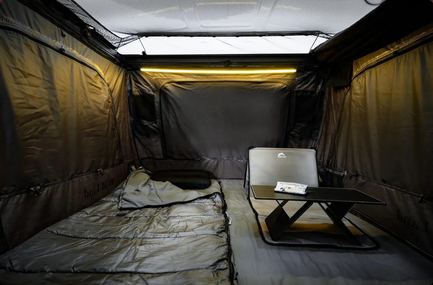 Compact living space with a bed, desk, and chair inside a vehicle or trailer.