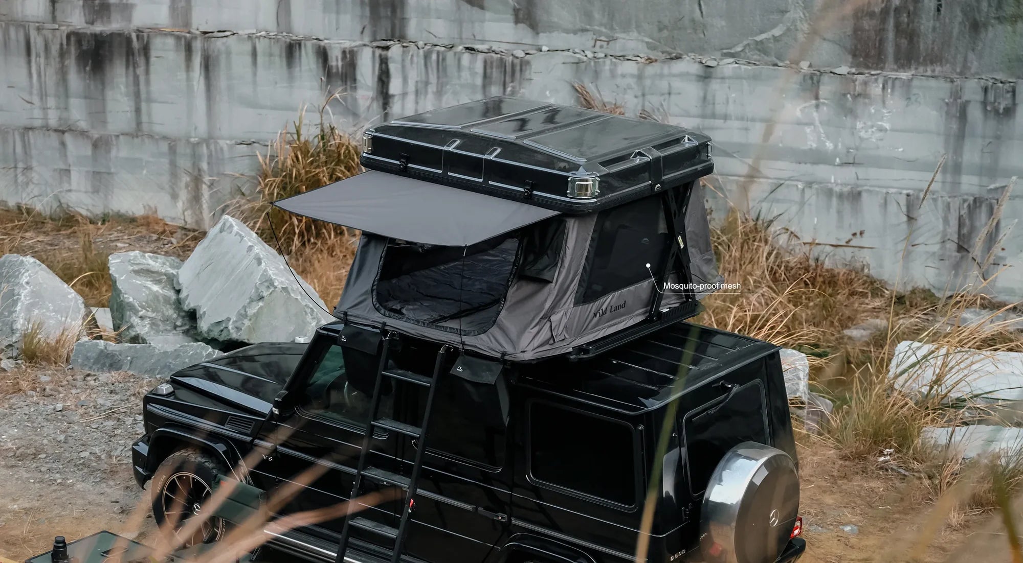 Black off-road vehicle with a rooftop tent in a rocky outdoor setting