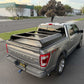 A silver Ford F-150 Platinum pickup truck parked outdoors in a parking lot, shown from the rear three-quarter angle. The truck bed is fitted with a black metal tonneau-style cargo bed cover and a black diamond-plate style panel on top.