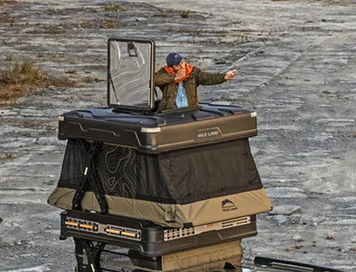 Person interacting with a large, portable outdoor kitchen unit on a rocky surface.