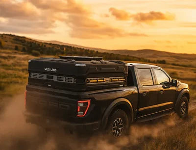 Black pickup truck with a bed cover driving on a dirt road during sunset.