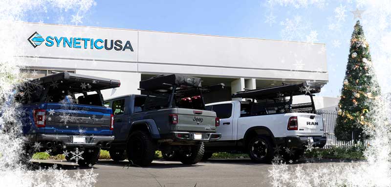 Three pickup trucks parked in front of a building with SYNETICUSA logo.