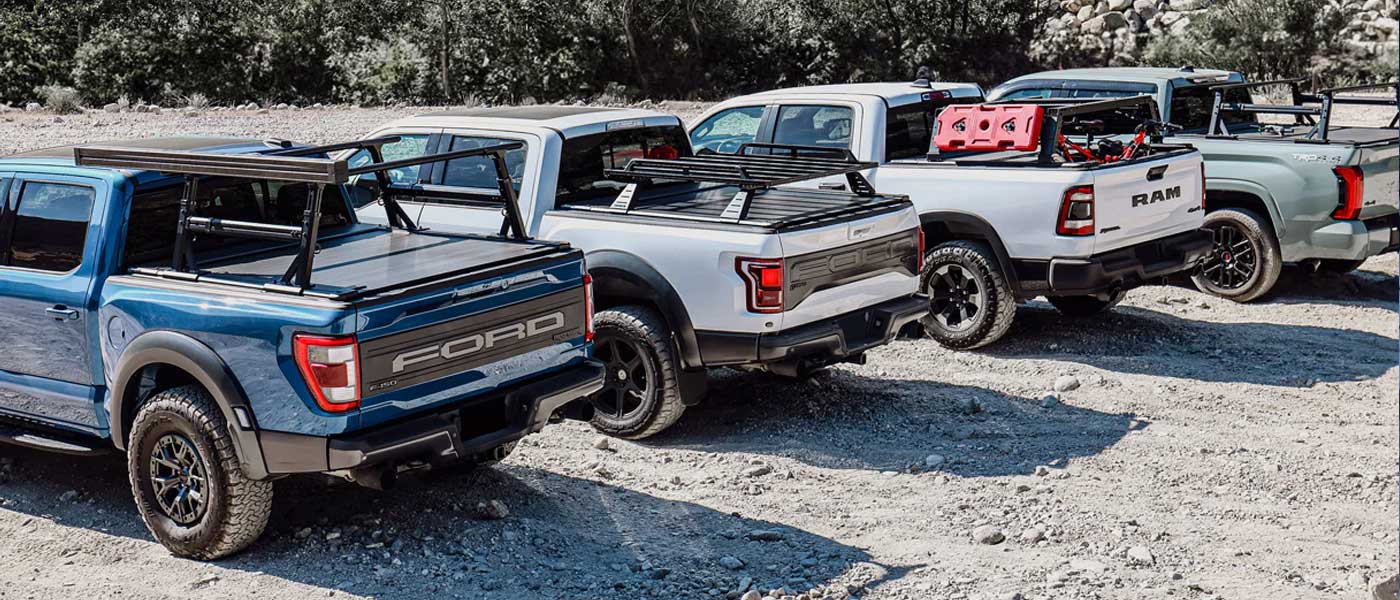 Row of pickup trucks with different models and colors on a gravel surface.