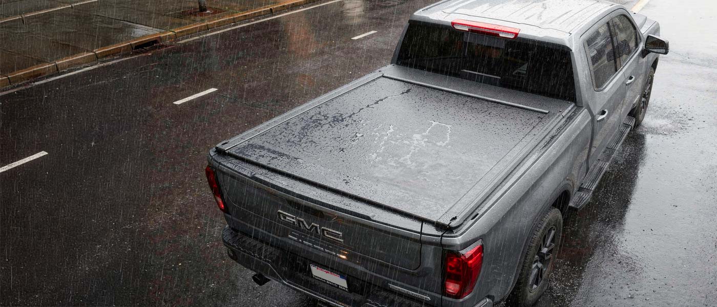 Gray GMC truck with a tonneau cover on a wet road