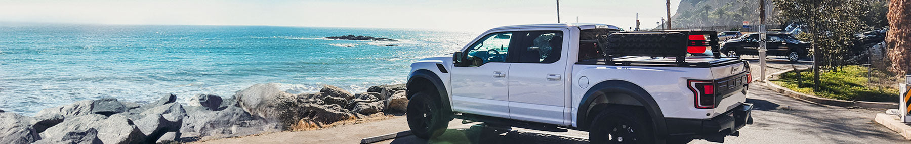 White f150 raptor truck on a road near a coastal area with ocean and rocks in the background