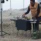 Person setting up a portable camping stove outdoors with a scenic background