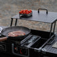 Portable outdoor cooking station with a pan on a stove, tomatoes, and a cutting board.