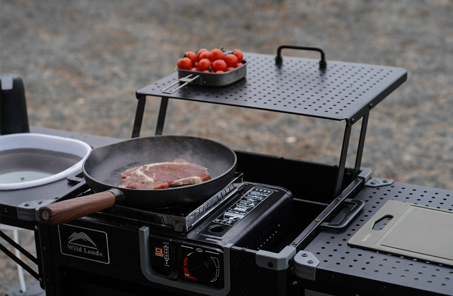 Portable outdoor cooking station with a pan on a stove, tomatoes, and a cutting board.