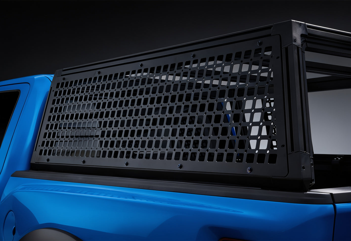 A black metal truck bed cargo cover with a grid pattern, mounted on the bed of a bright blue pickup truck against a dark studio background.