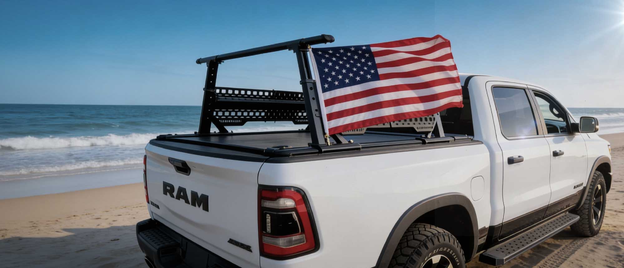 White RAM truck on a beach with an American flag on the back