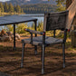 A green camp chair with fabric seat and back is shown outdoors beside a folding table, with a lake, trees, and mountains in the background.
