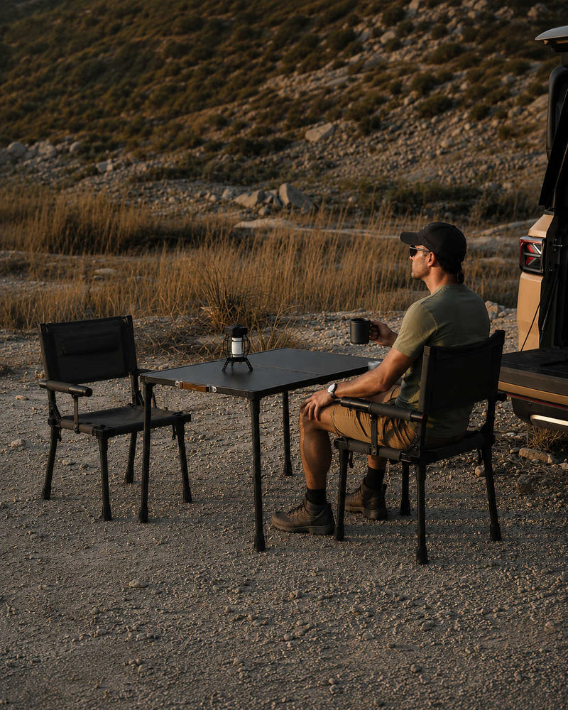Man sitting at a camping table with chairs in a desert setting